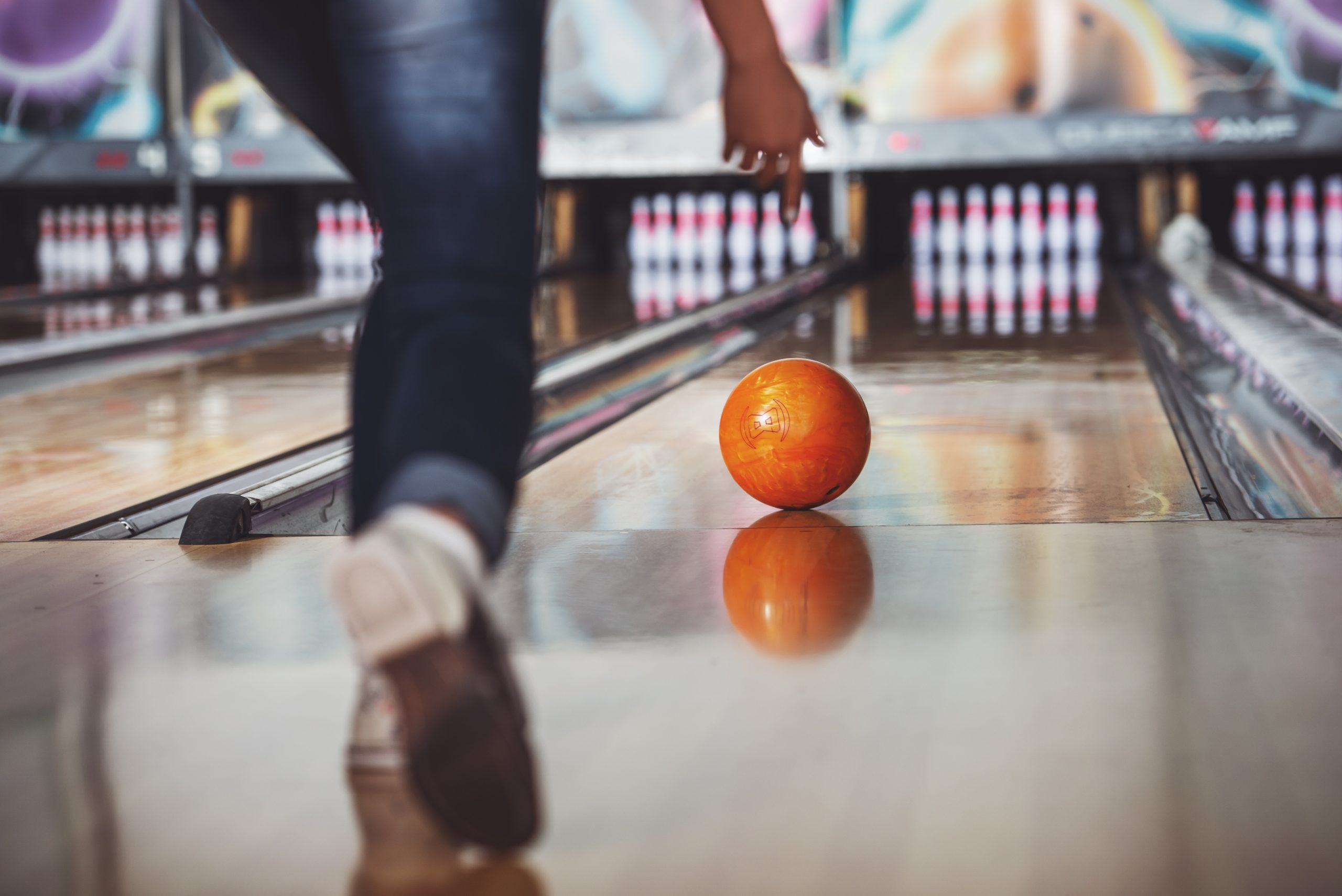 Girl bowling an orange bowling ball.